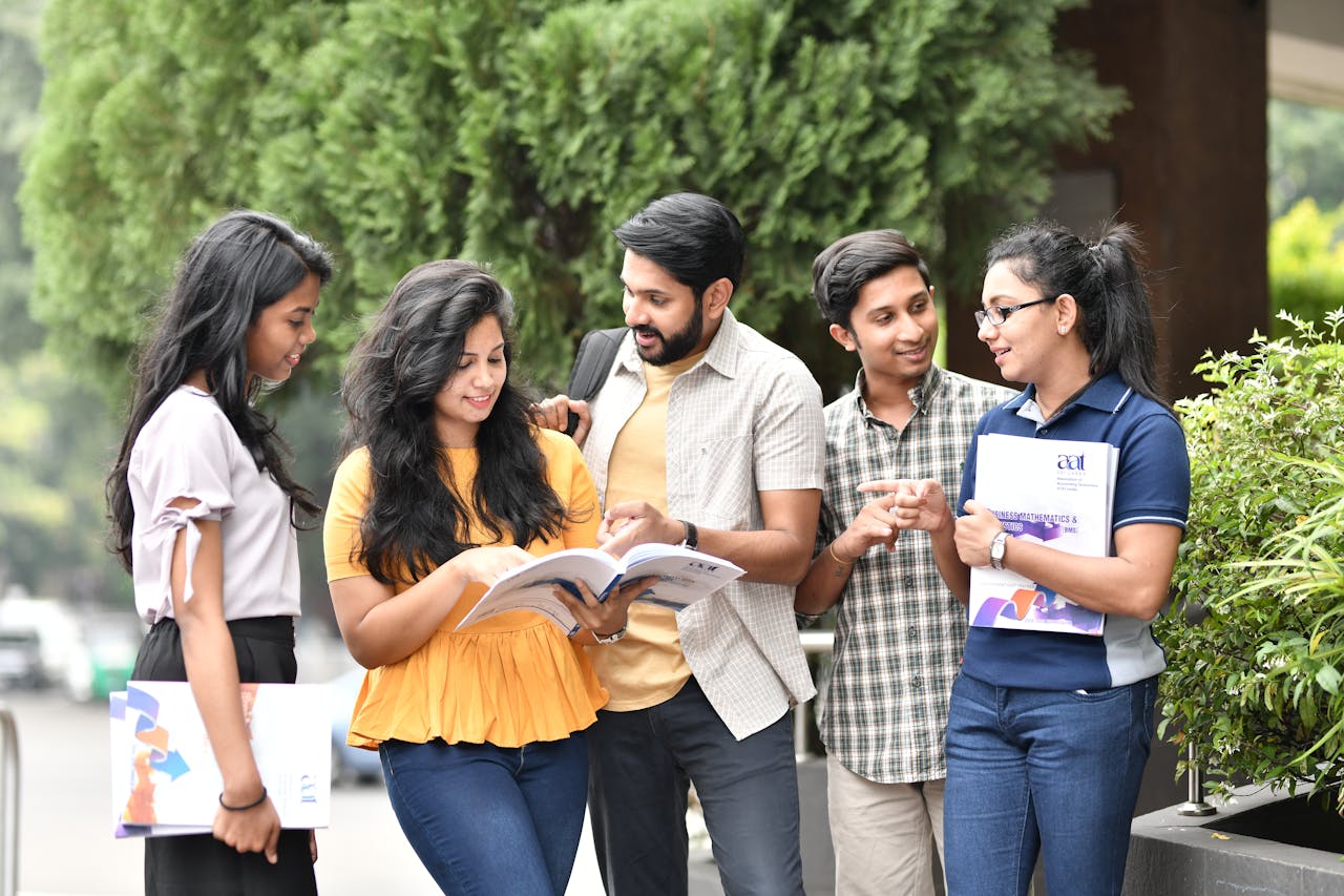 A group of diverse college students engaged in outdoor group study session, sharing books and ideas.